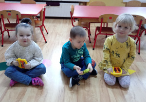 Dzieci siedzą trzymając instrumenty prekusyjne w dłoniach